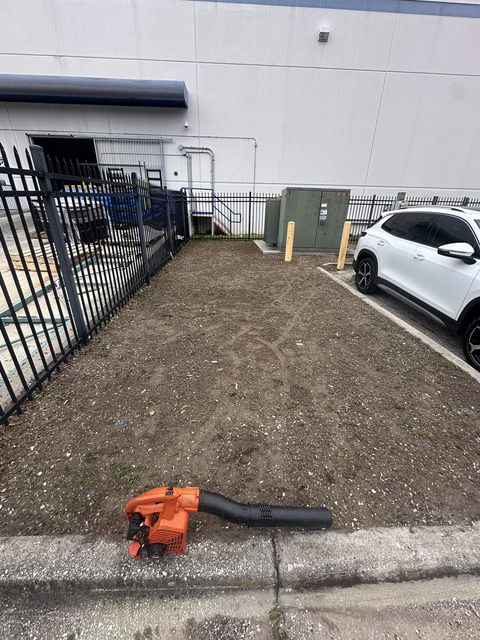 Commercial landscape strip cleared of weeds down to bare soil, with a leaf blower resting at the curb