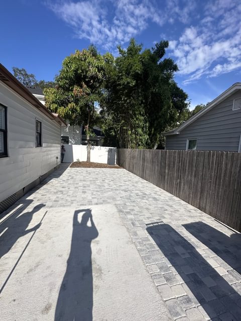 Entrada larga de adoquines grises a un costado de una casa blanca, junto a una cerca de madera, con árboles al fondo, en Tampa Bay