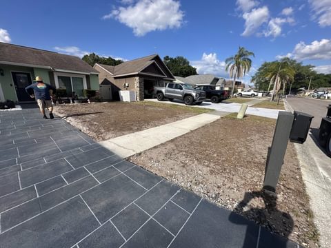 Jardín delantero nivelado y sin césped junto a una entrada de adoquines gris oscuro y un camino de concreto, antes de instalar el césped nuevo, en Tampa Bay